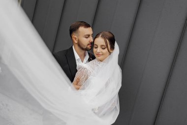 Güzel gelin damadı nazikçe kucaklıyor, damat da onu omuzlarından kucaklıyor. Düğün konsepti. Bir kadın ve erkeğin güzelliği ve şefkati.