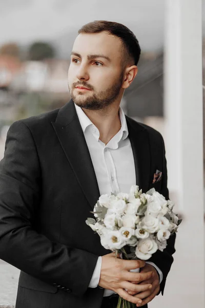 portrait of a handsome man with flowers in his hands on the balcony of a hotel room in the morning. Preparation for an event or a new working day. New opportunities, acquaintances. Close-up portrait
