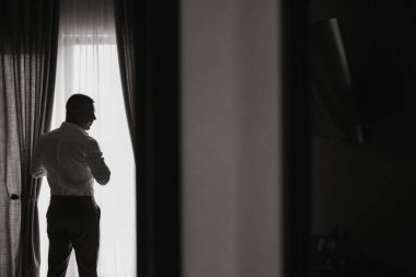 Rahat adam otel odasında doğal ışıkla beyaz gömlek giyer. Damat bir gömlek giyer ve düğün için hazırlanır. Boş alan