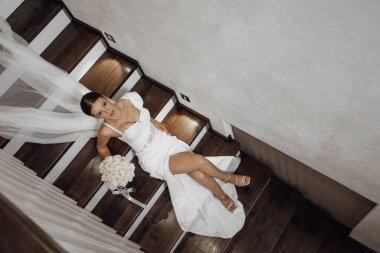 Güzel bir gelin, şık bir iç mekanda şık bir portre. Esmer gelin, düğün makyajlı ve saç stili olan beyaz gelinlik giyen mutlu kadın. Gelinin en iyi fotoğrafı. Yeni evliler