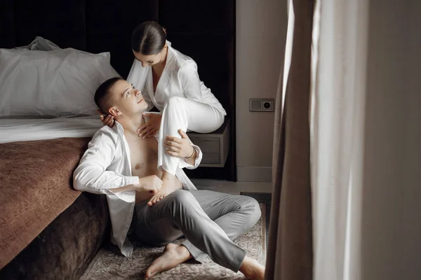 Sensual and tender morning of the bride and groom in the hotel room. Happy and in love brides and grooms. Confident girl bride and handsome boy groom. Preparation for the wedding