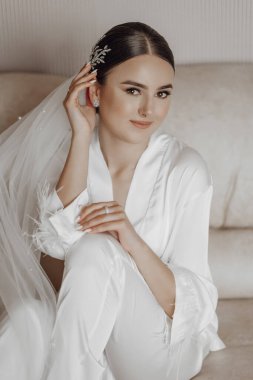 İpek takım elbiseli ve peçeli gelin odasında, kanepede oturuyor. Gelinin sabahı. Hazırlık. Düğün fotoğrafçılığı