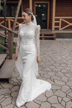 Portre. Şık, uzun bir elbise ve peçeyle gelin elinde buket, ahşap korkulukların yanında poz veriyor. Doğada düğün