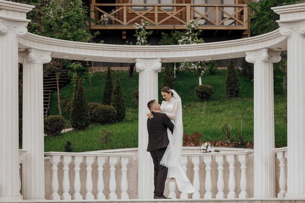 The bride and groom embrace near the Roman-style columns. An exquisite wedding