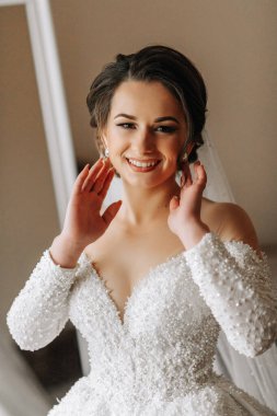 Gelinlik giymiş, uzun kollu bir gelin odasında poz veriyor. Gelinin sabahı. Hazırlık. Düğün fotoğrafçılığı