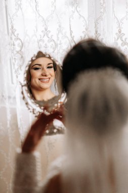 Gelinlik giymiş gelin odasında poz veriyor, aynaya bakıyor. Siyah beyaz fotoğraf. Gelinin sabahı. Hazırlık. Düğün fotoğrafçılığı