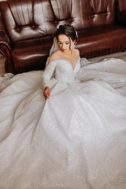 Gelin, uzun, şehvetli bir gelinlik içinde odasında yatağında poz veriyor. Uzun tren. Gelinin portresi. Omuzlarını ve yakalarını aç..