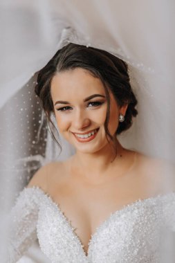 Düğün portresi. Gelin zarif bir gelinlik içinde duvağa sarılmış pozlar veriyor. Gelinin sabahı. Güzel saç ve makyaj.