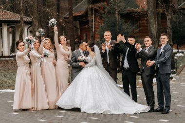 Gelin ve damat sarılıyor, arkadaşlarıyla poz veriyor. Arkadaşlar eğleniyor. Mutlu anlar. Doğada düğün portresi, açık renkli düğün fotoğrafı.