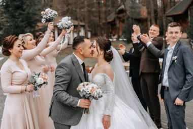 Gelin ve damat sarılıyor, arkadaşlarıyla poz veriyor. Arkadaşlar eğleniyor. Mutlu anlar. Doğada düğün portresi, açık renkli düğün fotoğrafı.