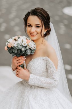 Trenli ve uzun peçeli beyaz elbiseli gelin, elinde buketle doğada poz veriyor. Yürü hadi. Doğada kış düğünü.