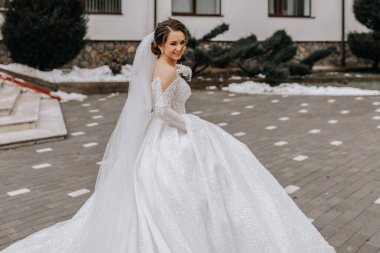 Trenli ve uzun peçeli beyaz elbiseli gelin, elinde buketle doğada poz veriyor. Yürü hadi. Doğada kış düğünü.