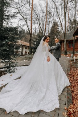 Portre. Gelin ve damat ormanda yürürken poz veriyorlar. Elbisenin üzerinde uzun bir tren. Kış düğünü