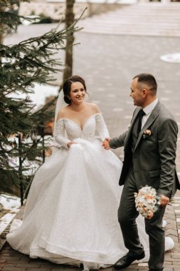 Portre. Gelin ve damat el ele tutuşurken yürürler ve poz verirler. Elbisenin üzerinde uzun bir tren. Kış düğünü