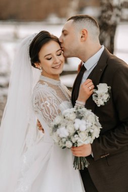 Gelin ve damadın düğün portresi. Doğada kış yürüyüşü. Gelin ve damat kucaklaşır ve öpüşürler. Enfes elbise.