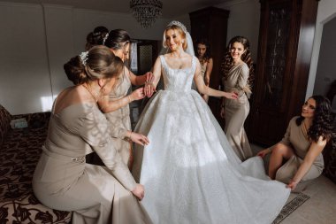 Beyaz elbiseli gelin, duvak ve krem rengi elbiseli kızlar, güzel ışık altında poz veriyorlar. Gelinin sabahı