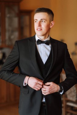 Beyaz gömlekli damadın siyah bir yelek iliklediği bir fotoğraf. İş stili. Şık bir saat.