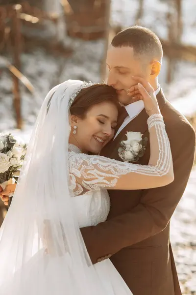 Wedding portrait of the bride and groom. Winter walk in nature. The bride embraces the groom, looking at each other.