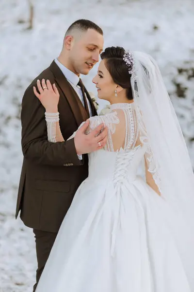 Wedding portrait of the bride and groom. Winter walk in nature. Bride and groom embrace and kiss. Exquisite dress