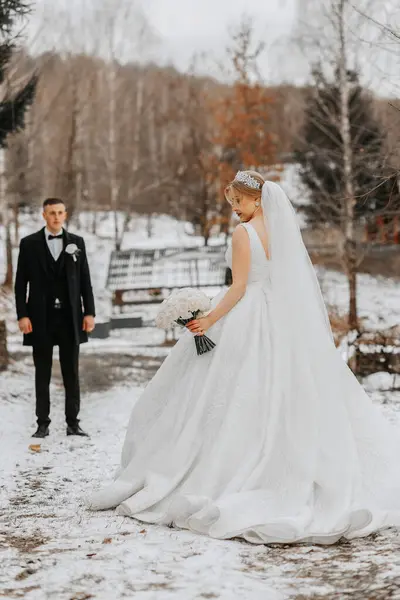 The bride and groom are walking in the winter garden. Winter photo session in nature. The groom is holding a bouquet.