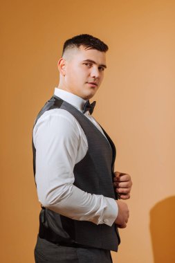 Beyaz gömlekli genç bir adam papyon takıyor ve siyah yelek giyiyor. Turuncu arka planda kısa saç stili olan damat siyah takımını giyer ve düğüne hazırlanır.