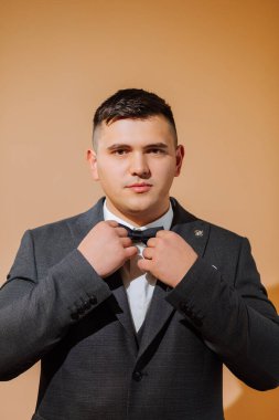 Beyaz gömlekli genç bir adam papyon takıyor ve siyah yelek giyiyor. Turuncu arka planda kısa saç stili olan damat siyah takımını giyer ve düğüne hazırlanır.