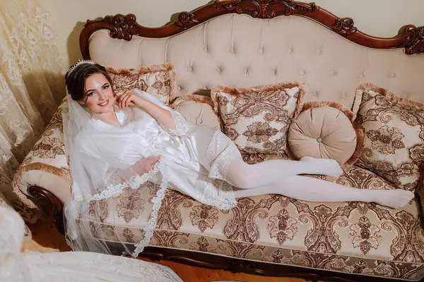 A young gorgeous bride is lying on an antique sofa. Full-length portrait. Preparing for the wedding. Morning of the bride.