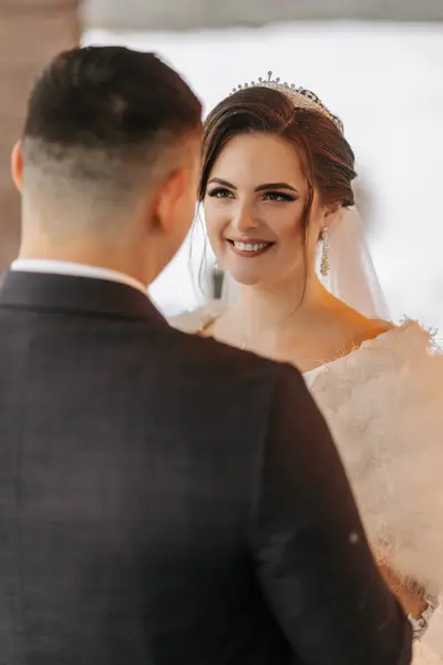 Beautiful wedding couple. Winter wedding of the groom in a beautiful suit and the bride in a beautiful wedding dress. Winter photo session of newlyweds. Tender look of the bride on the groom