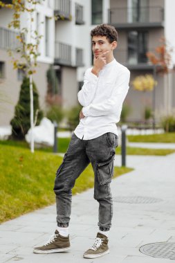 Gündelik giysiler içindeki bir gencin dikey yakın plan portresi. Sonbahar parkında gün ışığında mutlu bir genç. Güzel bir çocuk doğadaki kameraya bakar..