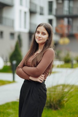 Dikey fotoğraf. Gayri resmi giyinmiş, tasasız, genç bir kız. Güzel bir kızın portresi bulanık bir geçmişi olan doğanın arka planına karşı..