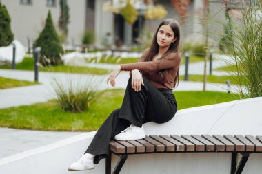 Dikey fotoğraf. Gayri resmi giyinmiş, tasasız, genç bir kız. Güzel bir kızın portresi bulanık bir geçmişi olan doğanın arka planına karşı..