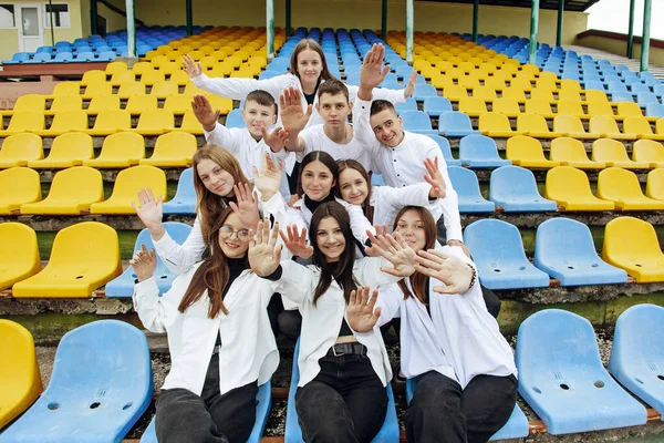 A group of many happy teenagers dressed in the same outfit having fun and posing in a stadium near a college. Concept of friendship, moments of happiness. School friendship