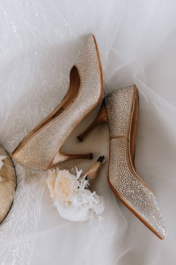 Gelinin nişan yüzüğü, şık topuklular, taze gül çiçekleri. Düğün detayları altın renginde.