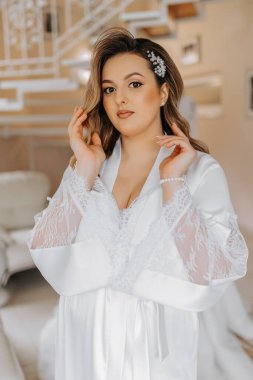 Gelinin düğünden önceki sabahı. Duvağı ve güzel bir saç stili olan güzel, genç bir kadın. Beyaz bir bornozla, harika bir iç mekanı olan bir odada. Doğal güzellik ve profesyonel makyaj..