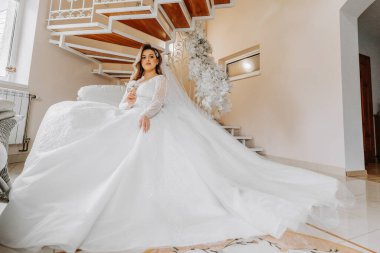 Şık bir gelinlik içinde, şık bir düğün saç stili ve profesyonel makyajlı güzel bir gelin. Sabahtan beri iç güzelliği olan bir odada genç ve güzel bir gelin. Yüksek kalite fotoğraf.