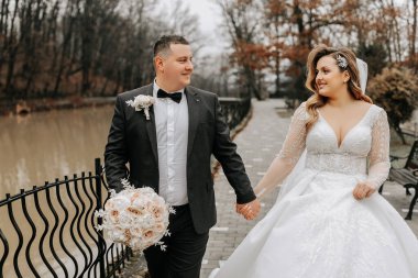 Gelin ve damat otelin yakınında yürüyorlar ve poz veriyorlar, mutlu ve günün tadını çıkarıyorlar, el ele tutuşuyorlar. Elbisenin üzerinde uzun bir tren. Kış düğünü