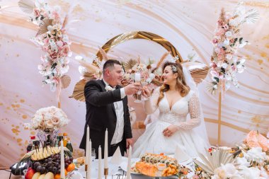 Güzel gelin ve damat düğünlerini bir partide kutluyorlar. Yeni evliler, çiçeklerle süslenmiş ve kurumuş çiçeklerle süslenmiş bir yemek masasında duran mutlu evliliğe kadeh kaldırır.