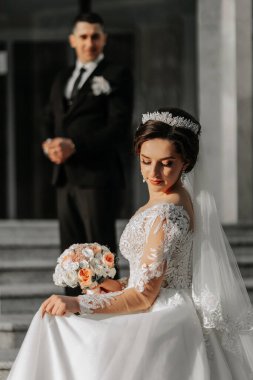 Gelin ve damat otelin yakınında yürüyorlar ve poz veriyorlar, mutlu ve günün tadını çıkarıyorlar, el ele tutuşuyorlar. Elbisenin üzerinde uzun bir tren. Kış düğünü