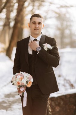 Siyah takım elbiseli yakışıklı ve erkeksi bir damat portresi. Kış mevsiminde doğada damat.