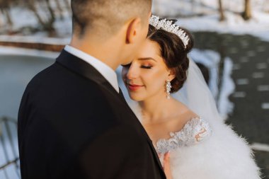 Kış düğünü. Düğün kıyafetleriyle yürüyen mutlu çift, düğün günlerinde kar altında kış parkında sarılıp gülümsüyor. Karlı kış havasında güzel bir çiftin kış aşkı hikayesi.