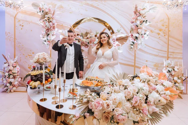 Beautiful bride and groom celebrate their wedding at a party. Newlyweds make a toast to a happy marriage, standing at a dining table decorated with flowers and dried flowers