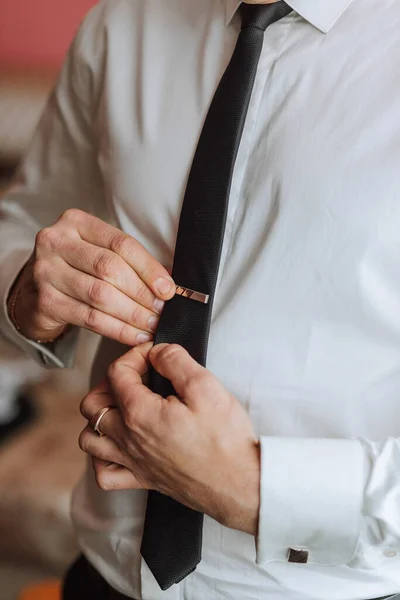 man's tie in hands, close-up photo of hands. The groom is preparing for the ceremony. Last preparations.