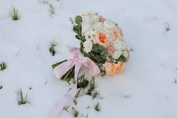 a wedding bouquet in a rustic style of various flowers and greenery, standing on the snow in winter.