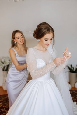 Gelinin sabahı. Gelinin baş nedimesi gelinin elbisesini bağlar, düğmelerini ya da kollarını bağlar. Kız arkadaşlar gelinin elbisesini bağlamasına yardım edin.