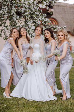 Gelin ve nedimelerin toplu portresi. Gelinlik giymiş bir gelin ve gümüş elbiseli nedimeler düğün günlerinde şık buketler tutarlar..