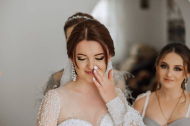 Gelinin sabahı. Gelinin baş nedimesi gelinin elbisesini bağlar, düğmelerini ya da kollarını bağlar. Kız arkadaşlar gelinin elbisesini bağlamasına yardım edin.