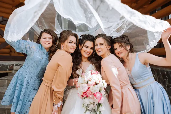 Group portrait of the bride and bridesmaids. A bride in a wedding dress and bridesmaids in beautiful dresses hold the bride's bouquet on the wedding day.