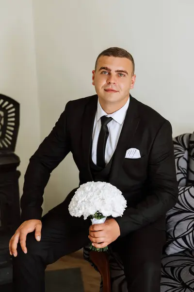 Stylish portrait of the groom with a bouquet of flowers. A man is preparing for a wedding ceremony in the morning. Groom's morning. Preparation for the groom's morning. Young and handsome groom.