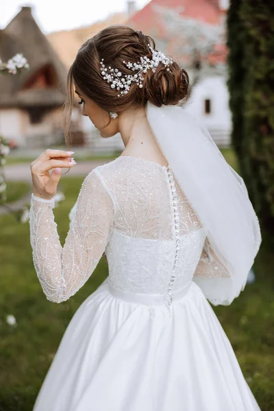 A red-haired bride in an elegant dress with long sleeves and a beautiful ornament in her hair, posing with her shoulders turned to the camera. Spring wedding