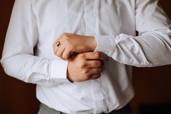 handsome business man buttoning shirt sleeves at home. The groom is preparing for the wedding. Close-up photo.